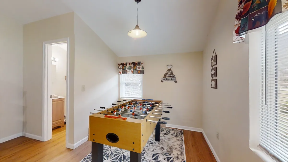 A bright and lively foosball table area with natural light flooding the room, wall art, and a window that hints at the outdoors. The setting is ideal for socializing, playing games, and fostering group fun.