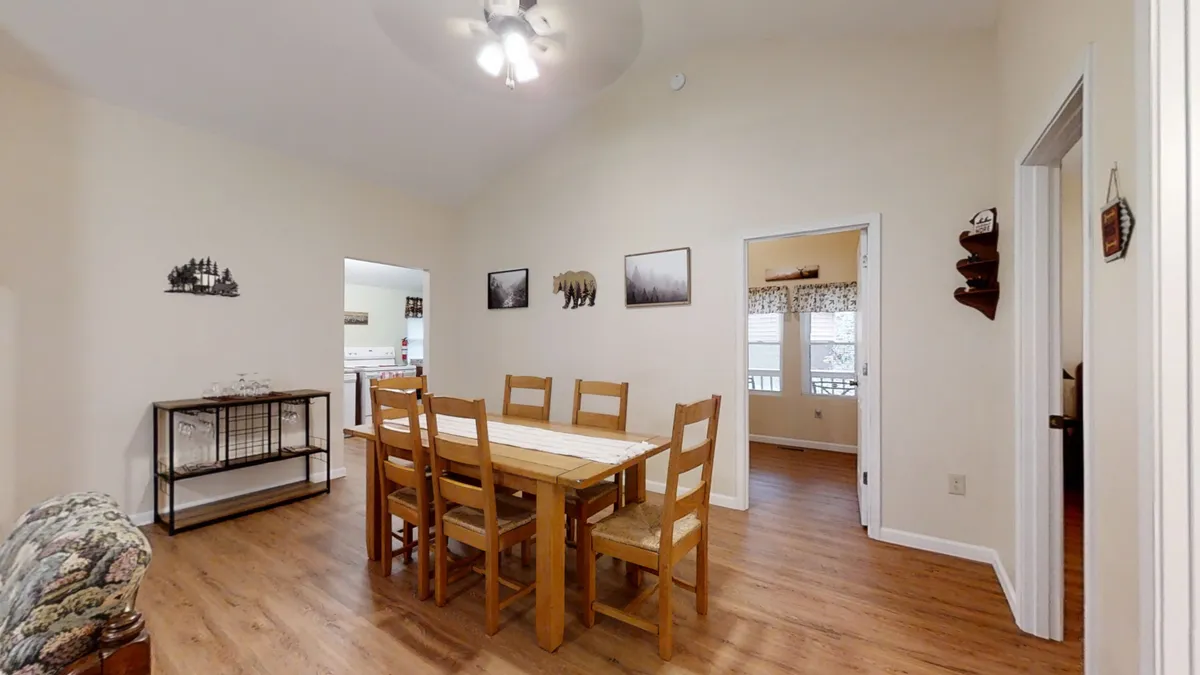 This image showcases a welcoming dining area featuring a rustic wood-top table surrounded by wooden chairs, decorative wall art, and an open doorway that hints at the home's spacious flow. The table is set for a gathering, creating an inviting atmosphere for family meals, board games, or lively conversation.