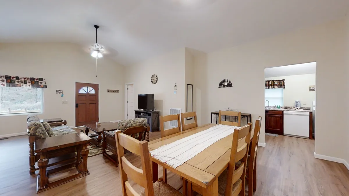 The image features a welcoming dining and living area with seating and a prominent view of the front door. The layout is open and airy, inviting guests and their pets to come inside after exploring outside. The arrangement encourages group gatherings and easy movement in and out.