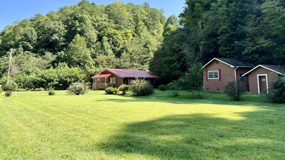 This wide exterior shot shows two houses flanked by an expansive green lawn and surrounded by trees, offering a clear look at the large, flat yard. The scene is serene, ideal for recreational activities, family gatherings, or simply soaking in the peaceful Smoky Mountain atmosphere.