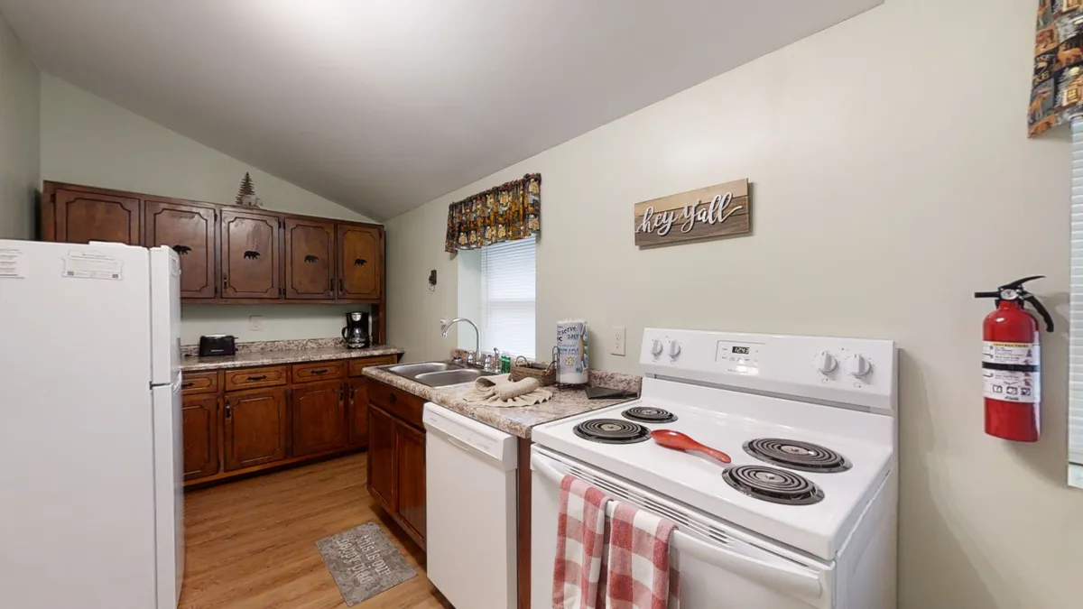 A cozy, well-equipped kitchen with a stove, wooden cabinets, a kitchen sink, and a charming decorative sign. The space is inviting for meal preparation and family gatherings, suggesting both practicality and comfort.