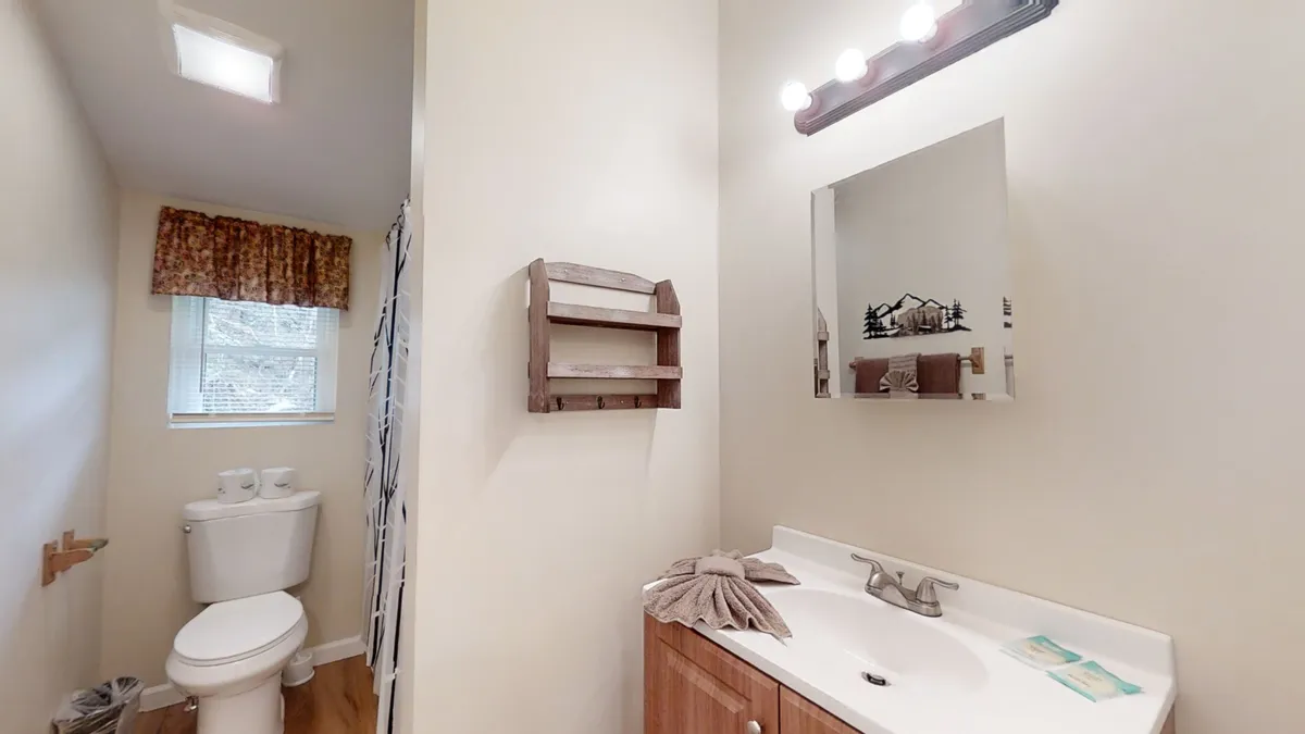 A functional, bright bathroom with a vanity and sink, mirror, toilet, and a shower/tub combo with a curtain. Natural light streams in from a window, giving the room a calm and refreshing feel.