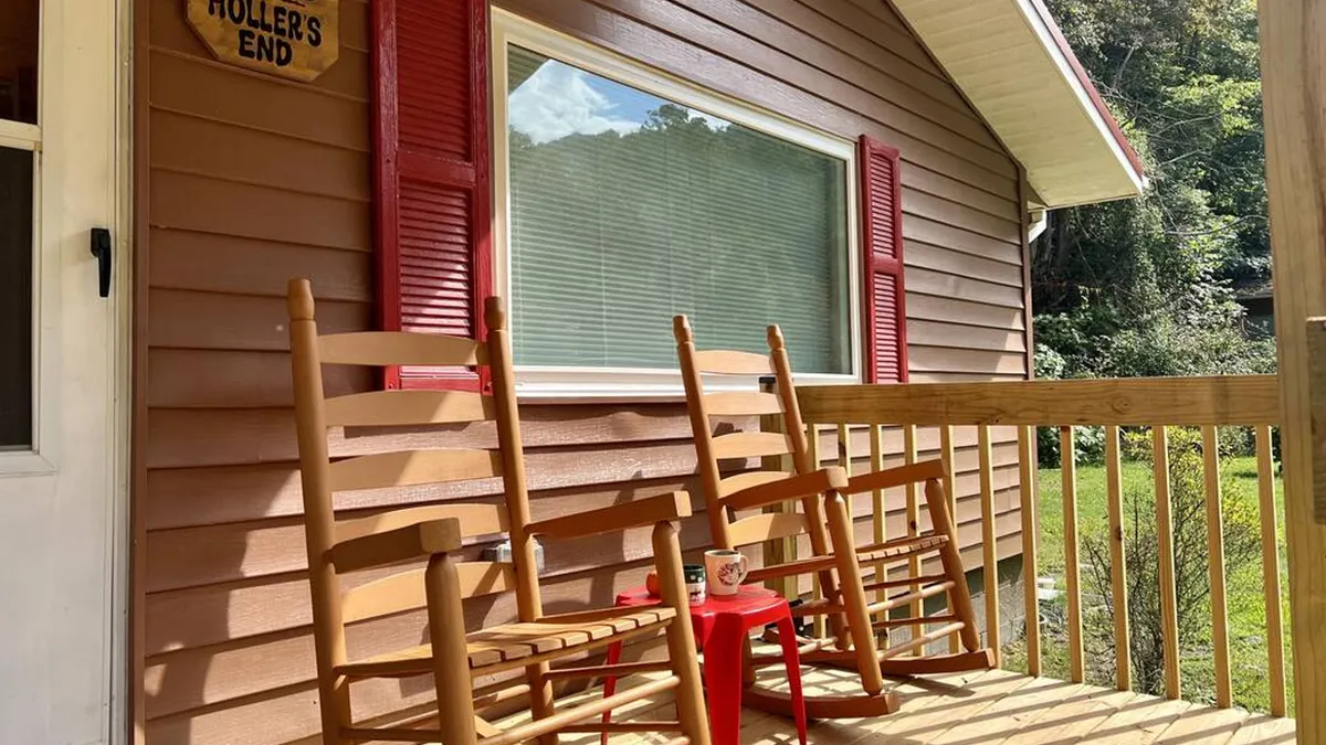 Another angle of the exterior porch, featuring comfortable rocking chairs and a red accent table, all set against the natural surroundings. The scene emphasizes connection to nature and a laid-back, communal vibe ideal for storytelling or simply soaking in the views.