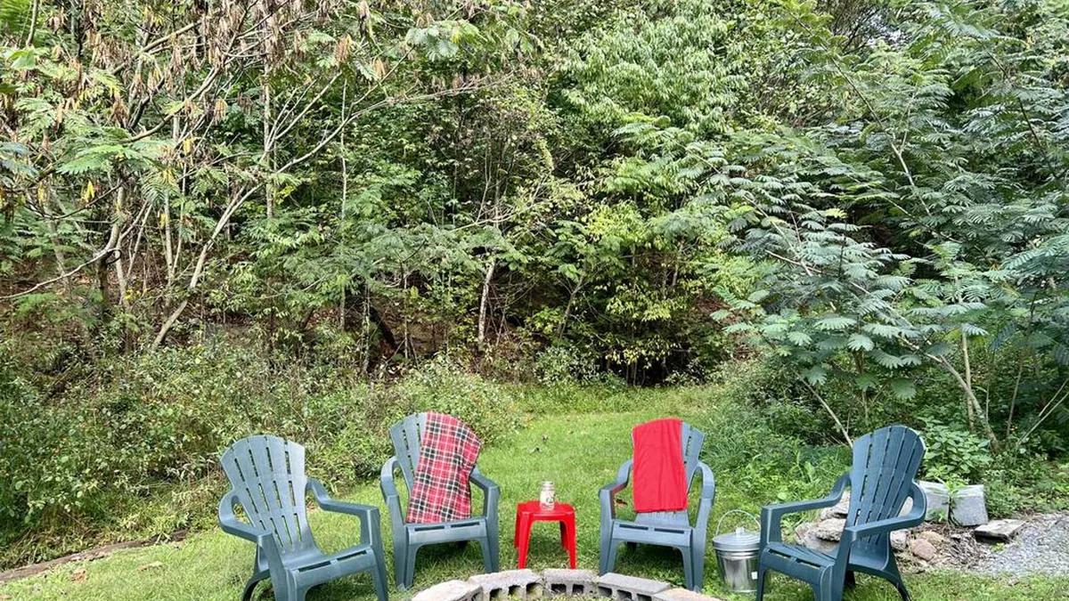 This image captures an inviting backyard fire pit area, surrounded by Adirondack chairs and a plaid blanket draped over one chair. The setup encourages campfire gatherings, storytelling, and stargazing, all set against a backdrop of greenery that connects guests to the peaceful outdoors.