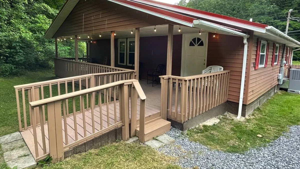 This inviting exterior features a front porch with outdoor seating, a ramp, and a visible entrance—showcasing the transition from inside to outside. The porch is perfect for sipping coffee in the morning or winding down in the evening, with easy access to the yard and walkways.