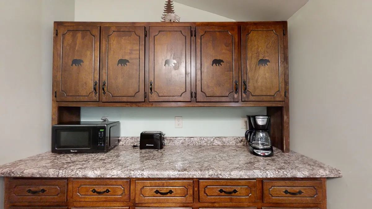 This image features wooden cabinets with charming bear motifs, a sleek granite countertop, and essential appliances like a coffee maker and microwave. The cozy, rustic details evoke the warmth and character of a mountain retreat.