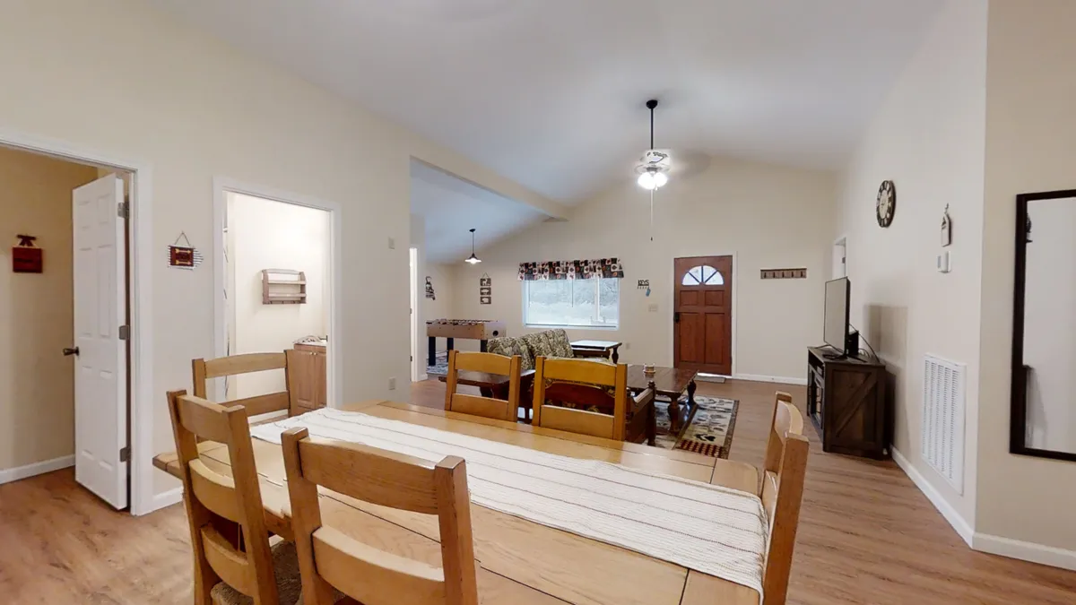 This image shows the cabin's open-plan living area and dining space, with a clear view of the front door. The room is cozy and well-lit, highlighting easy access to the outdoors. The inviting atmosphere suggests a seamless transition between indoor relaxation and outdoor adventure.
