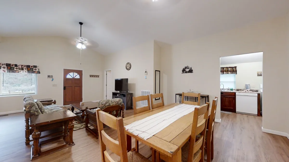 An interior shot showing a dining table adjacent to the living room seating, with the entrance door and kitchen entry visible. The arrangement emphasizes the easy flow between spaces, ideal for shared meals and keeping everyone connected.