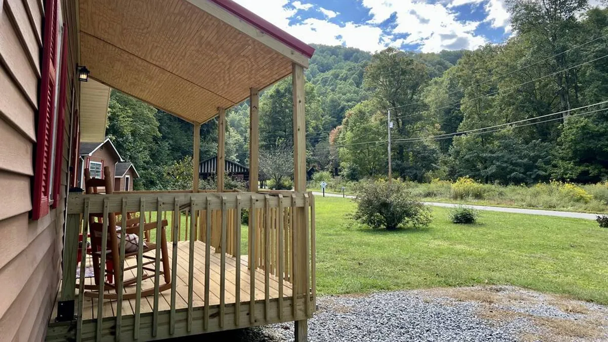 A wide wooden porch with classic rocking chairs overlooks a scenic mountain view. The peaceful setting highlights opportunities for relaxation while staying engaged with the natural beauty around the cabin.